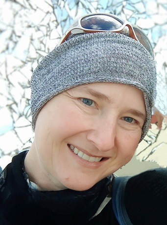 Me, a white agender person smiling against a mirror background